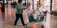 Bildet er fra kjøpesenteret Charlottenbergs Shoppingcenter og viser en dame i grønn strikkejakke med en handlekurv full av ulike bæreposer.