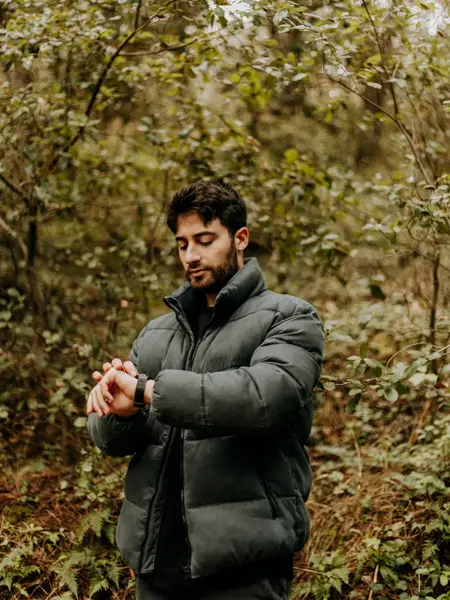 Mann med stor og tykk grønn boblejakke ser på klokka ute i skogen 