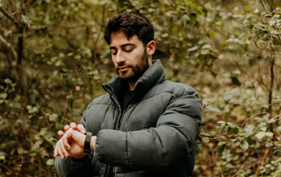 Mann med stor og tykk grønn boblejakke ser på klokka ute i skogen 