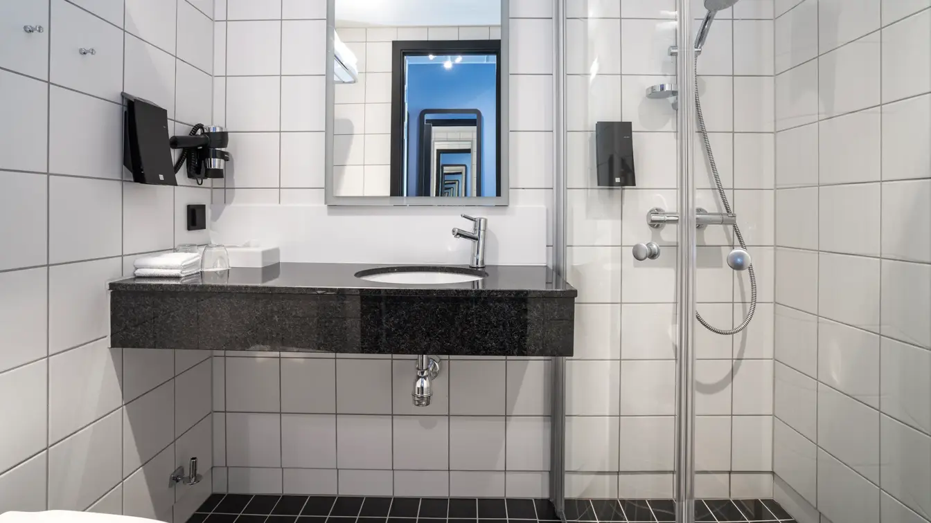 Hvite veggfliser, svarte gulvfliser, vask, speil, dusj, såpe