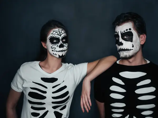Loving couple with skull face art in costume of skeletons on dark background, Halloween theme
