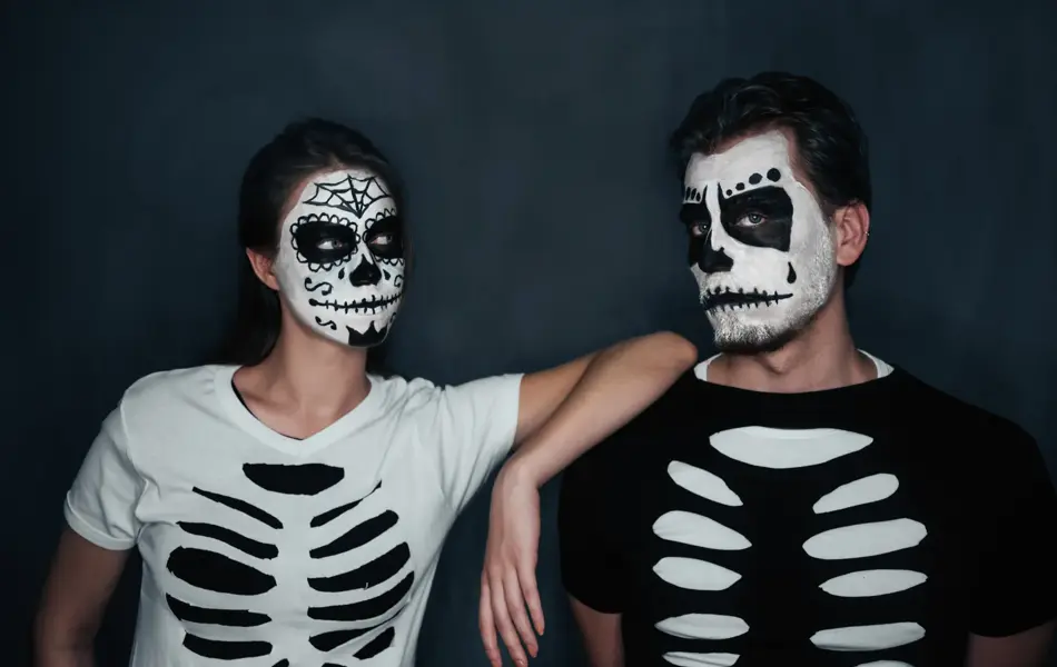 Loving couple with skull face art in costume of skeletons on dark background, Halloween theme