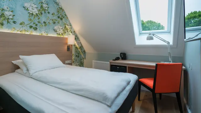 Seng og skrivebord under skråtak på standard enkeltrom på Thon Hotel Tønsberg Brygge