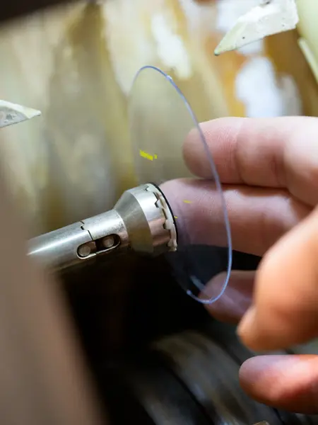 Fingre holder et brilleglass i en slipemaskin