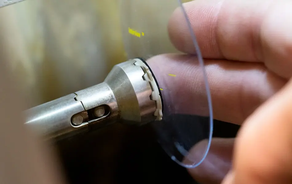 Fingre holder et brilleglass i en slipemaskin