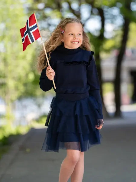 Jente står ute og holder et flagg i mørk blå kjole.