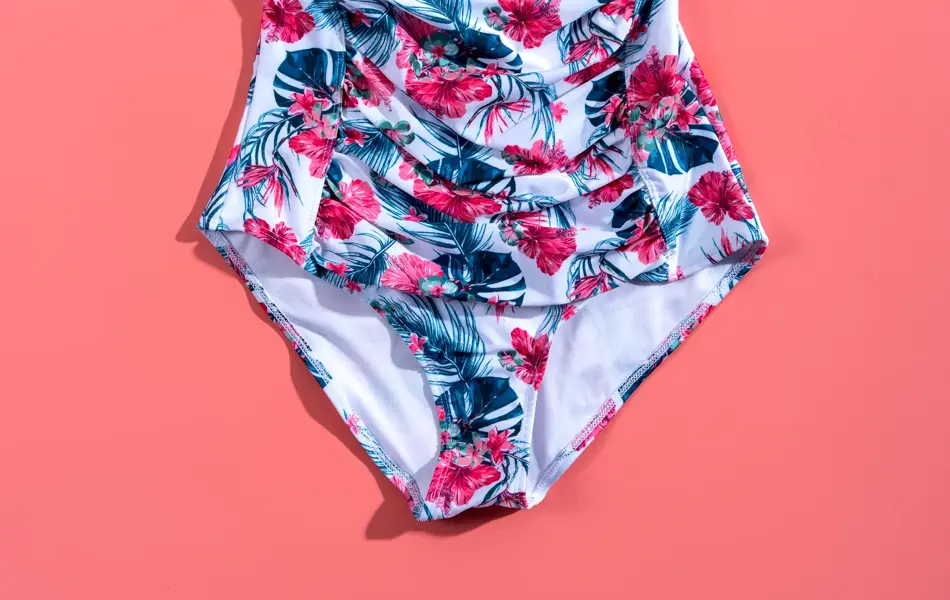 Hvit, burgunder og grå badedrakt på rosa bakgrunn