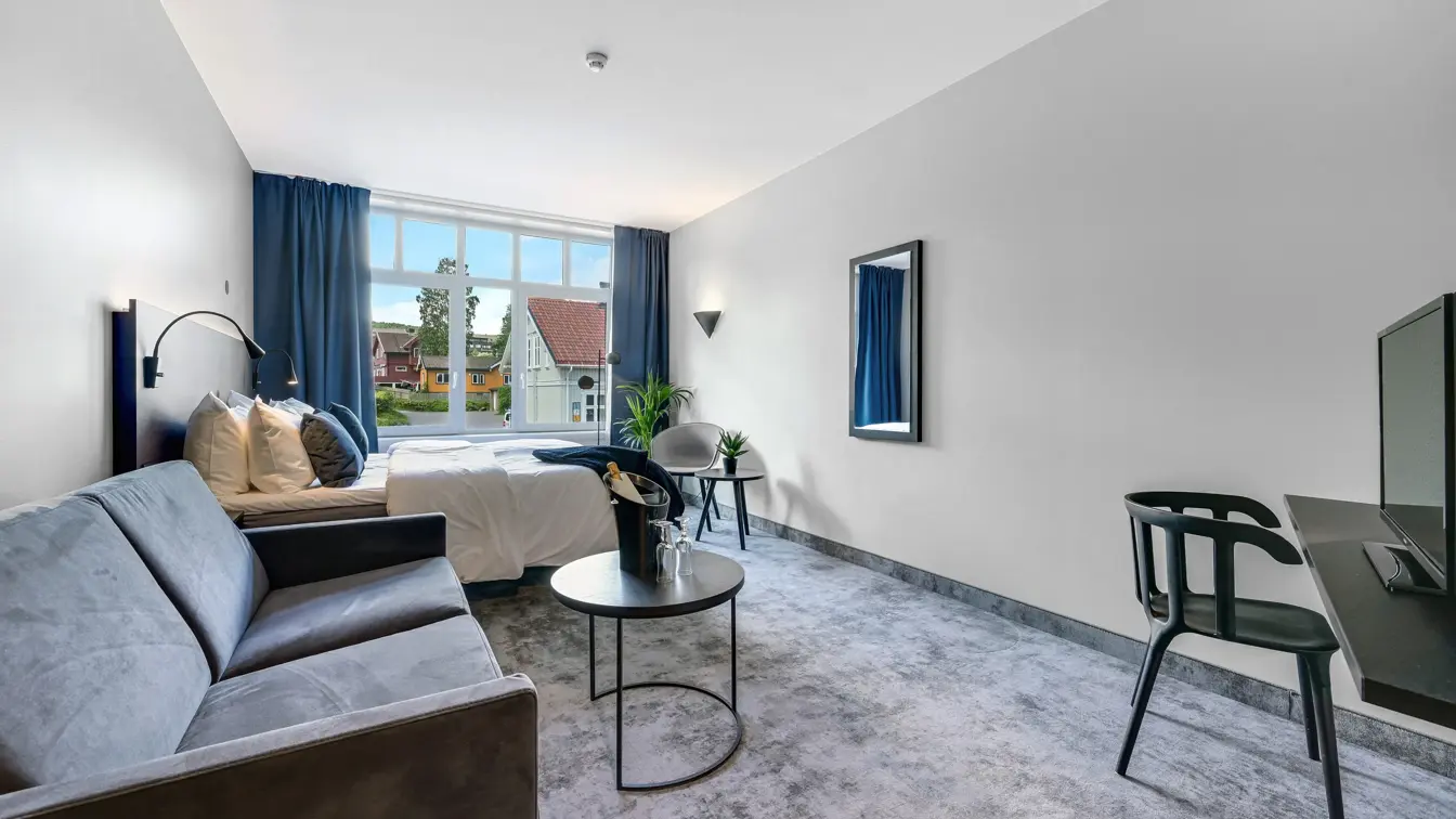 Dobbeltseng, grå sofa, salongbord, lenestol, salongbord, vindu, blå gardiner 