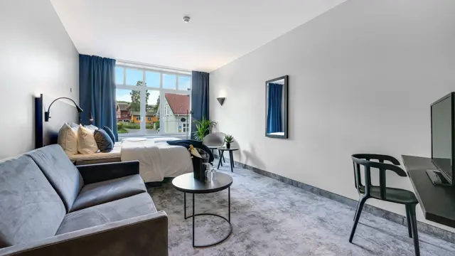 Dobbeltseng, grå sofa, salongbord, lenestol, salongbord, vindu, blå gardiner 
