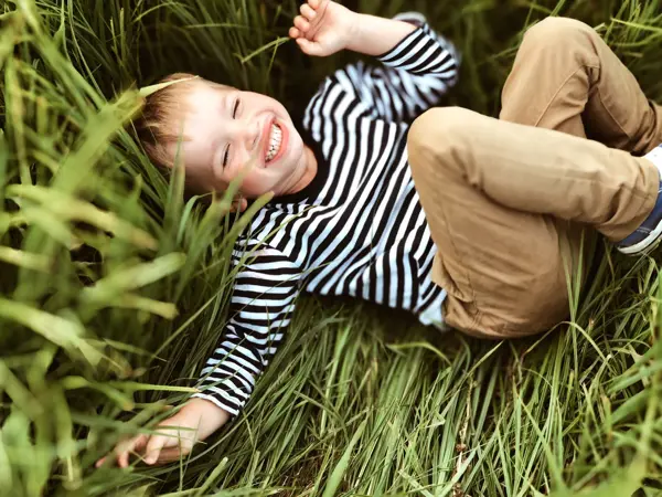 Gutt ler og ligger i gresset iført stripete genser og beige bukse
