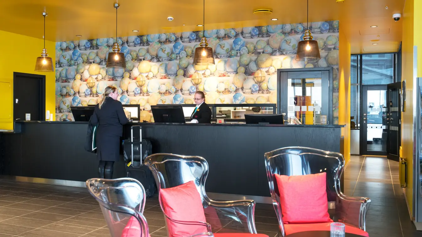 Gjest sjekker inn hos resepsjonist med tapet med globuser i forskjellige farger på Thon Hotel Kirkenes ved kaia i Kirkenes sentrum