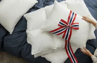 Hvite dundyner og -puter på en seng, med sløyfe i norske flaggfarger.