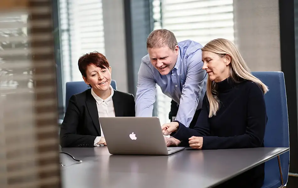 tre kollegaer som ser sammen på en pc skjerm på et møterom
