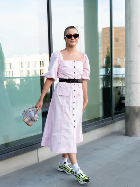 Ung kvinne som smiler til kamera og poserer i rosa kjole, sneakers og solbriller