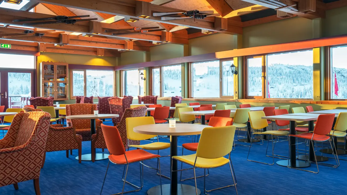 Spiseplass med fargerike stoler, stort maleri av skeikampen på veggen og store vinduer som ser ut mot landskapet på Austlid fjellstue