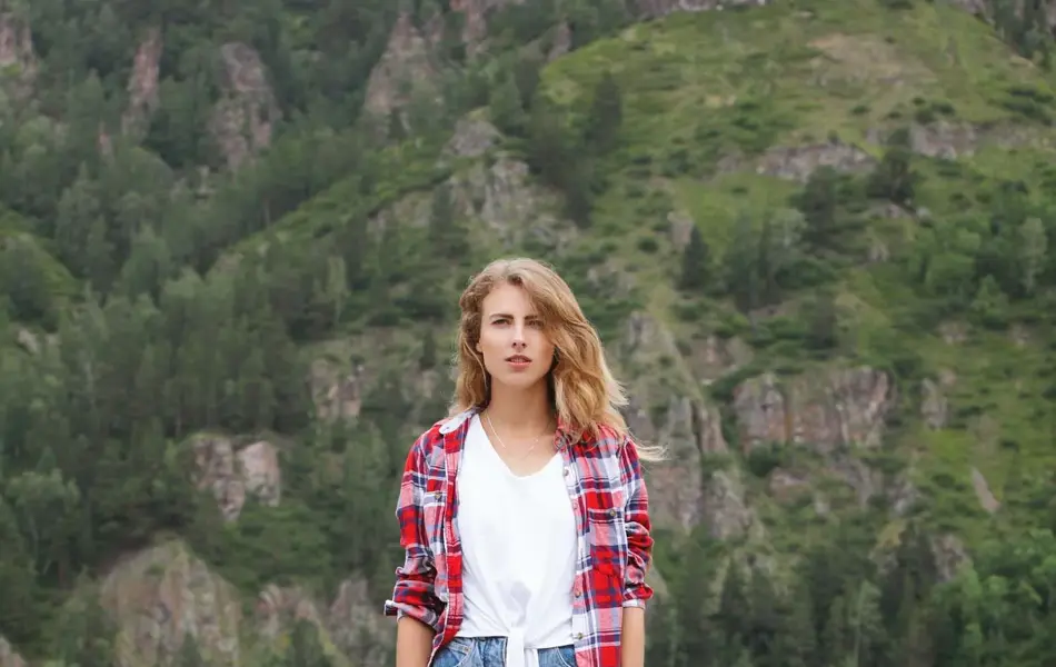 Jente med rød flanellskjorte og olashorts står på skateboard på brygge 