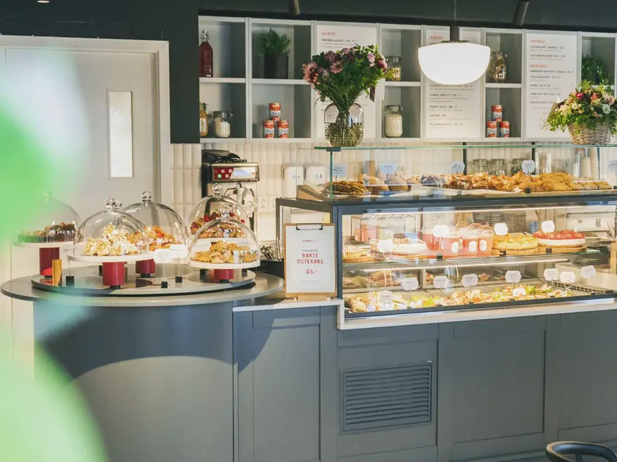 grå-disk-med-kaker-bak-glassvegg-og-hyller-med-blomster-i bakgrunnen