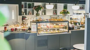 grå-disk-med-kaker-bak-glassvegg-og-hyller-med-blomster-i bakgrunnen