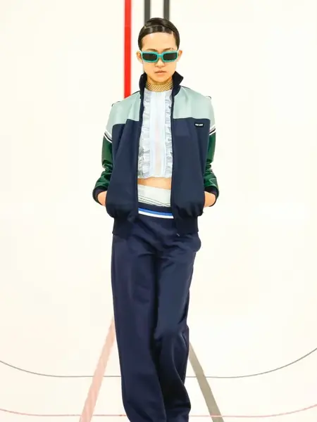 Dame på catwalken med en mørkeblå og intgrønn joggedress og en hvit topp inne i joggedressjakken