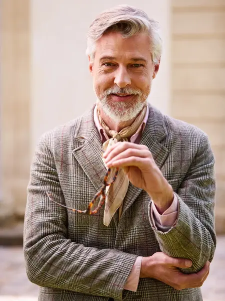 Mann med briller, rosa skjorte og silketørkle i halsen ser i kamera 