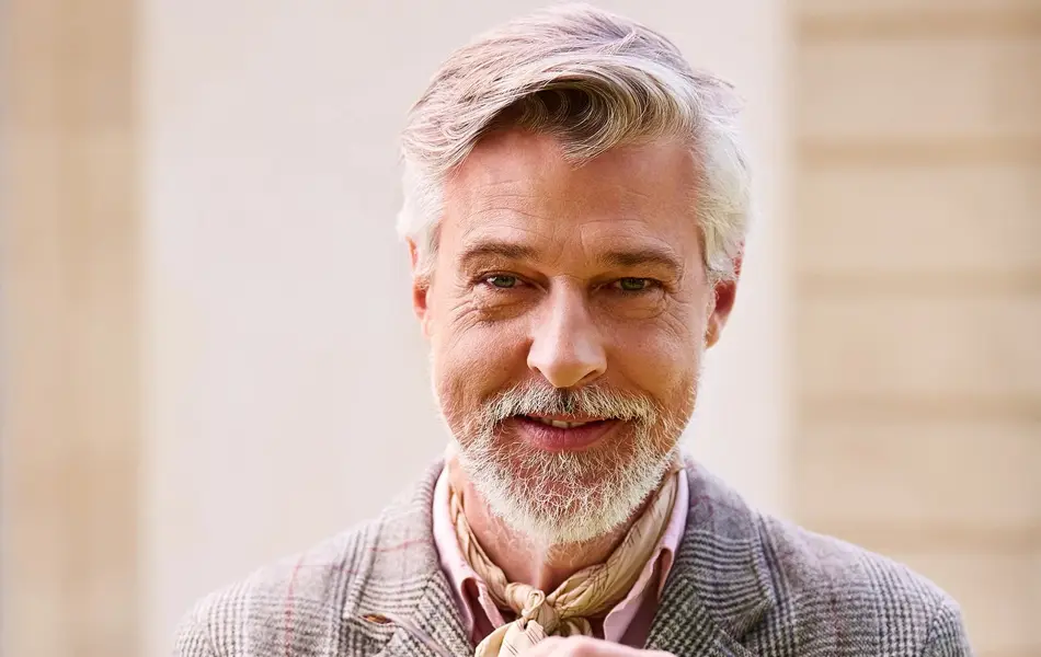 Mann med briller, rosa skjorte og silketørkle i halsen ser i kamera 