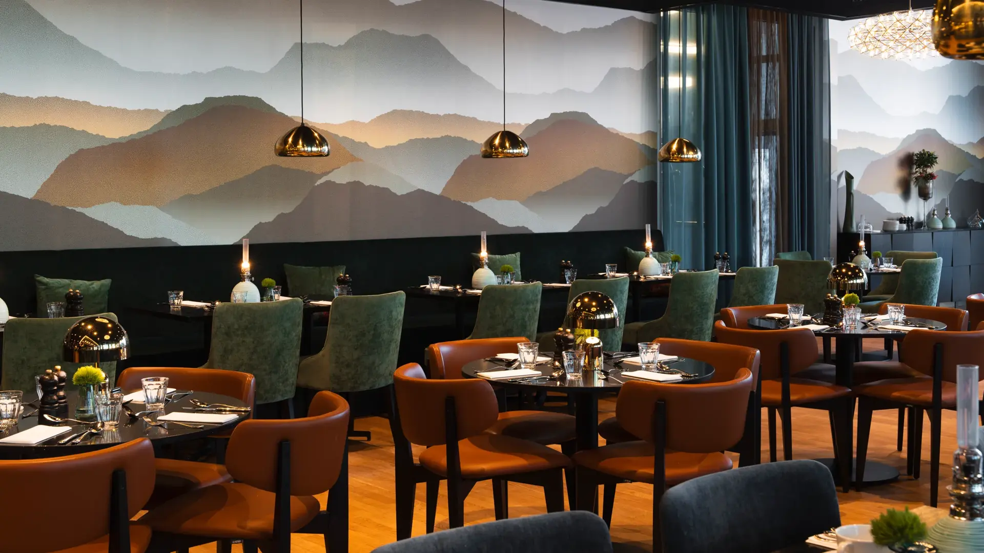 Sitteplasser i restaurant. Runde bord med tilhørende brune skinnstoler og sittebenk langs veggen med tilhørende bord og grønne stoler.