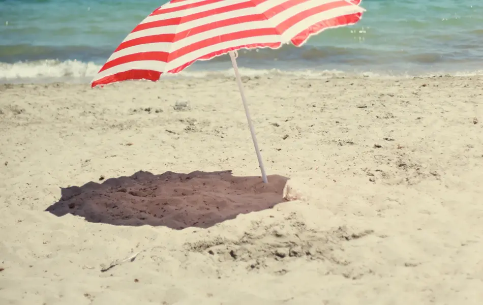 A red and white striped beach umbrella on the beach.     