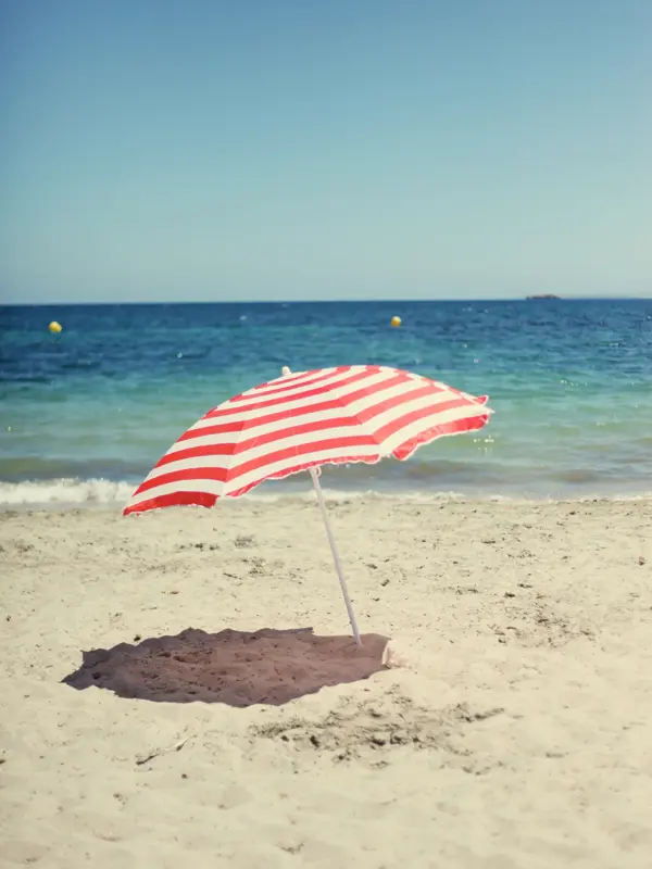 A red and white striped beach umbrella on the beach.     