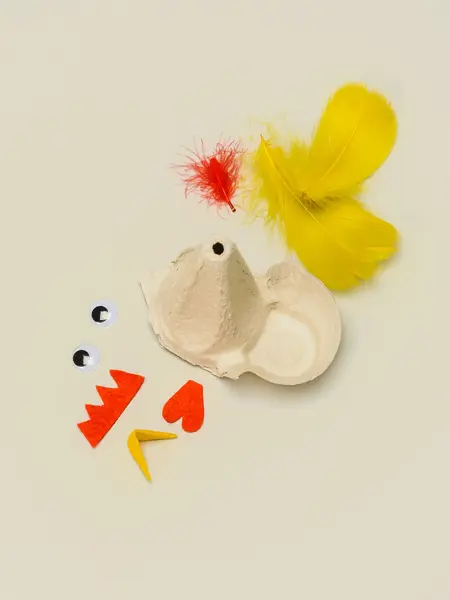 En del av en eggekartong, fjær i rød og gul, egg, og stoffbiter klippet ut