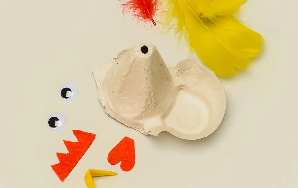 En del av en eggekartong, fjær i rød og gul, egg, og stoffbiter klippet ut
