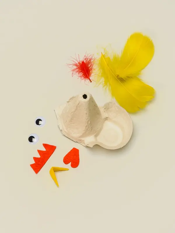 En del av en eggekartong, fjær i rød og gul, egg, og stoffbiter klippet ut