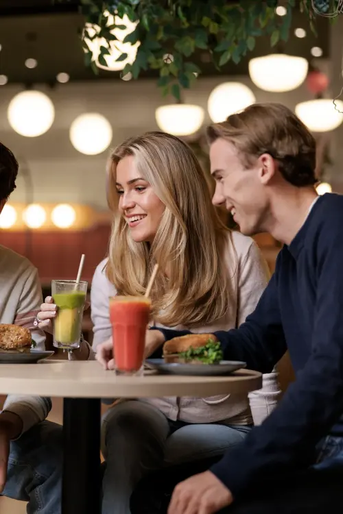 To gutter og en jente som sitter ved et bord i en kafé og ser på mobilen den ene gutten holder i hånden