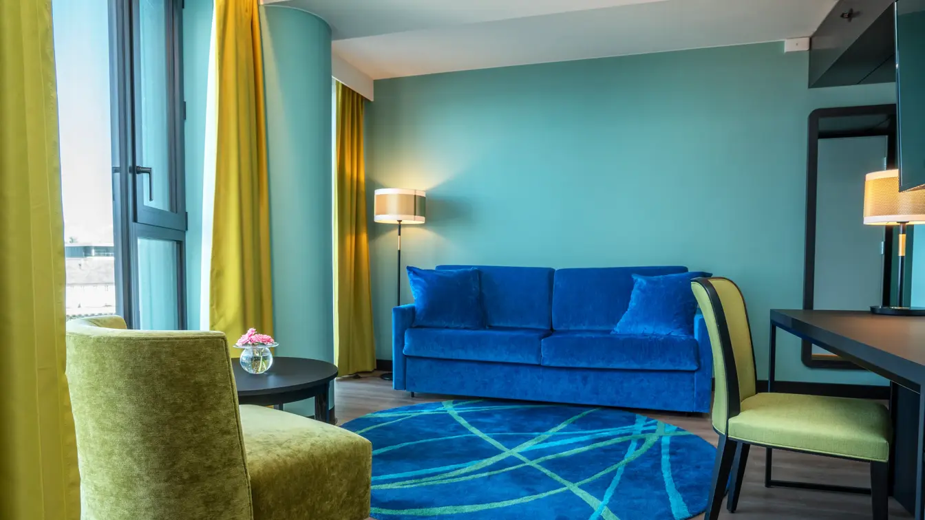 Skrivebord, blå sofa, vindu, gule gardiner, gul lenestol, salongbord, turkis vegg