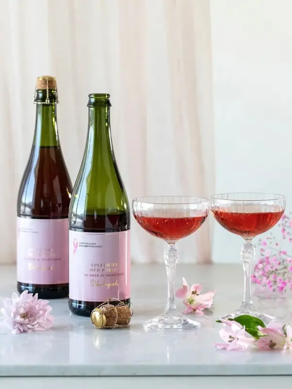 To flasker cider og to glass med cider på et bord, rosa blomster som pynt